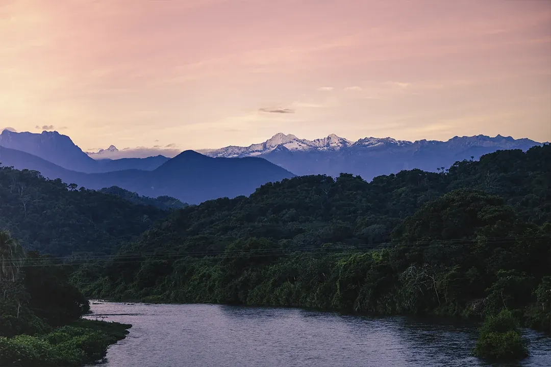 Los picos nevados de la Sierra Nevada al atardecer, sobre el bosque y el río