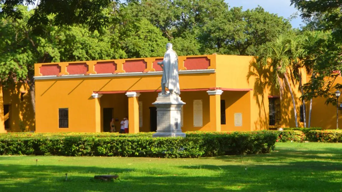 La casa quinta colonial, amarilla, con el monumento en el jardín